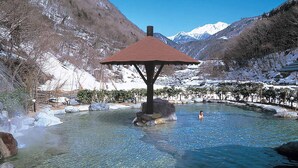 Una piscina cristalina con un pabellón de madera en el centro, rodeada de montañas y árboles cubiertos de nieve.