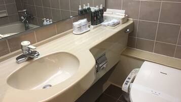 A modern bathroom with a large sink, a toilet, and a mirror. There are toiletries on the counter and a paper towel dispenser.