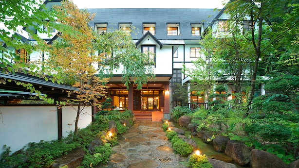 Un edificio tradicional japonés con un camino de piedra que conduce a la entrada, rodeado de exuberante vegetación y rocas.