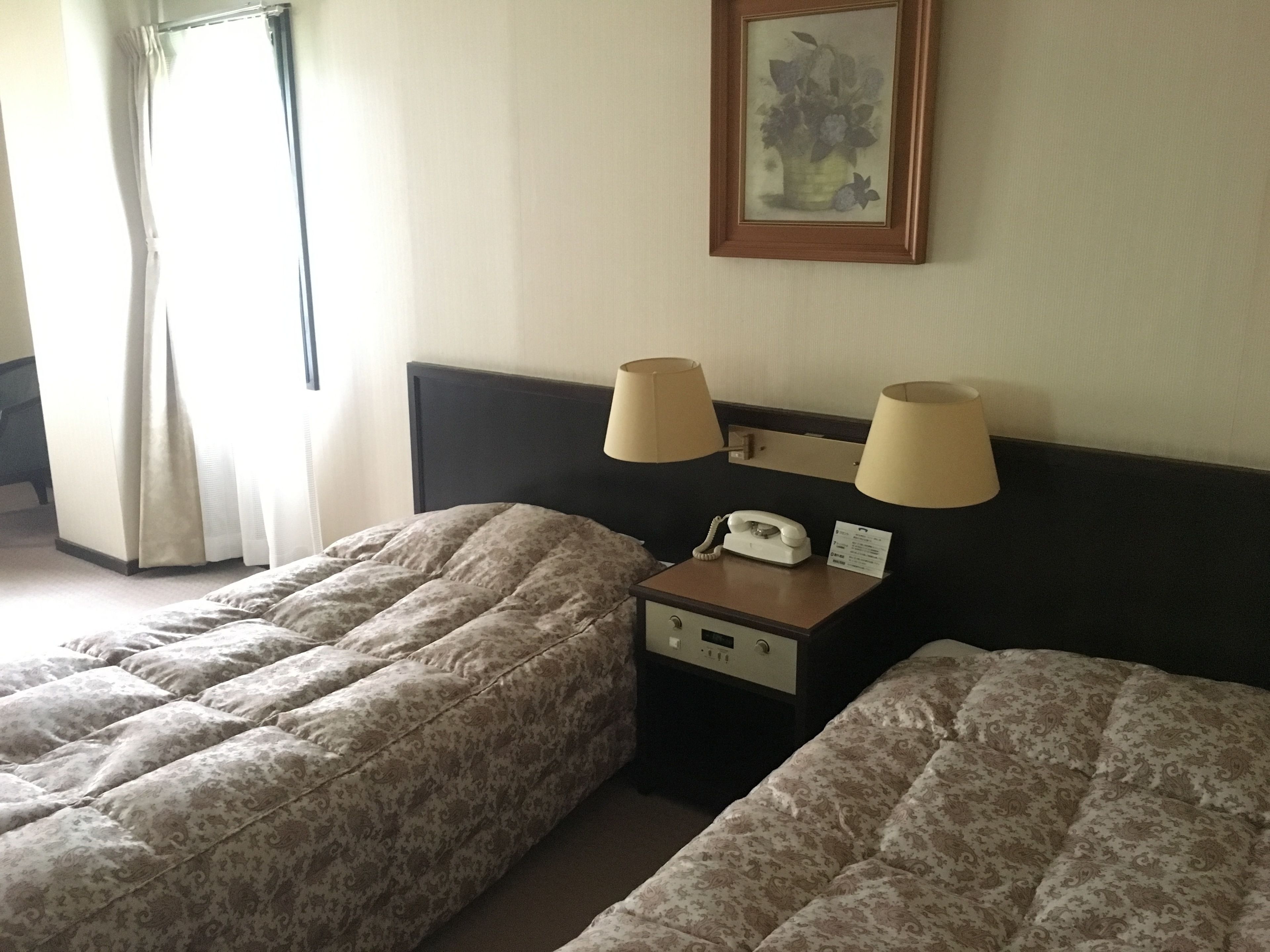 A hotel room with two beds, a nightstand with a telephone and a lamp, and a framed picture on the wall.