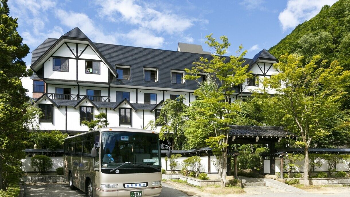 Un immeuble à plusieurs étages, avec un autobus garé devant, entouré de verdure et bordé d’une architecture traditionnelle.