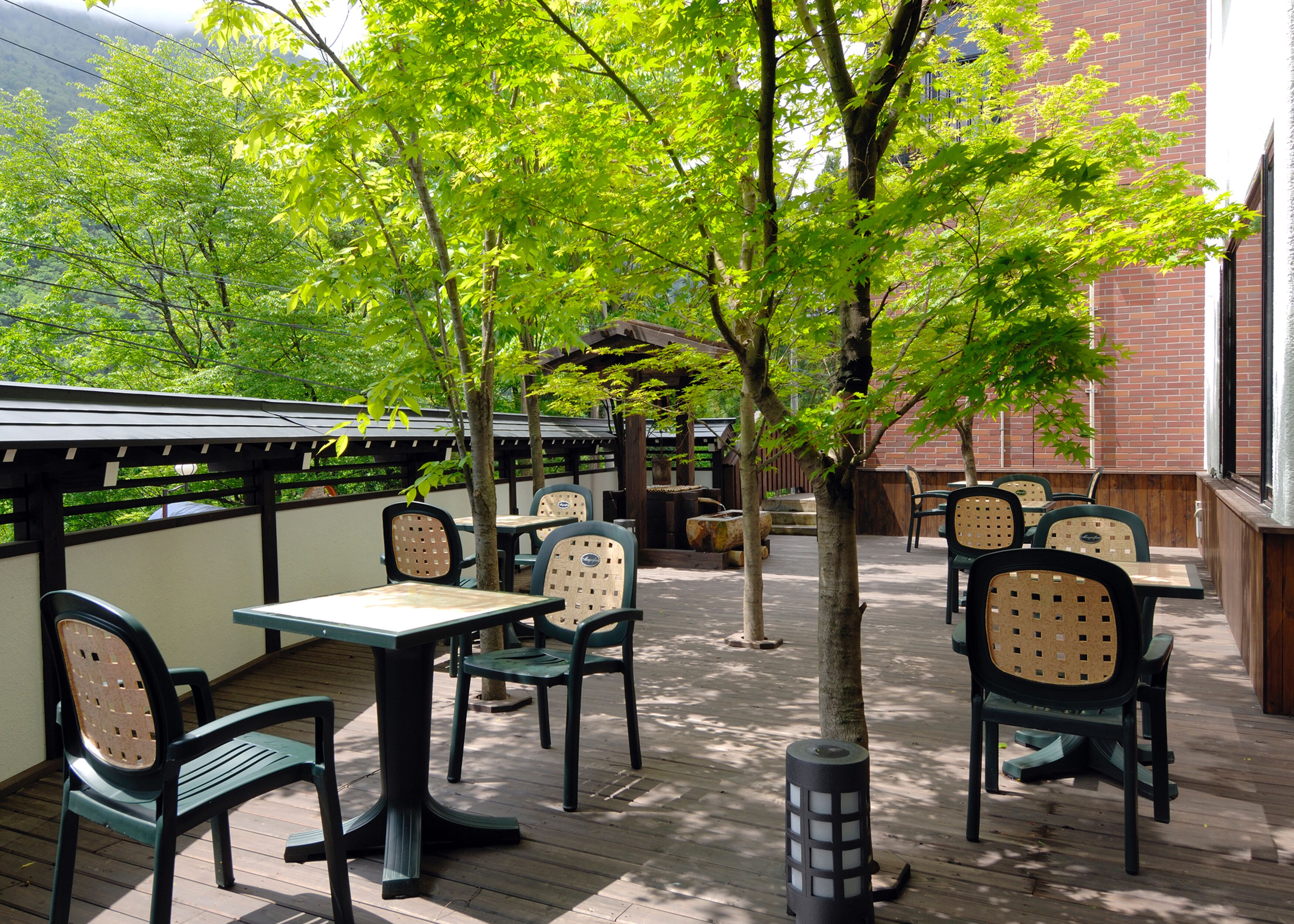 An outdoor patio area with tables and chairs, surrounded by trees and a brick wall.