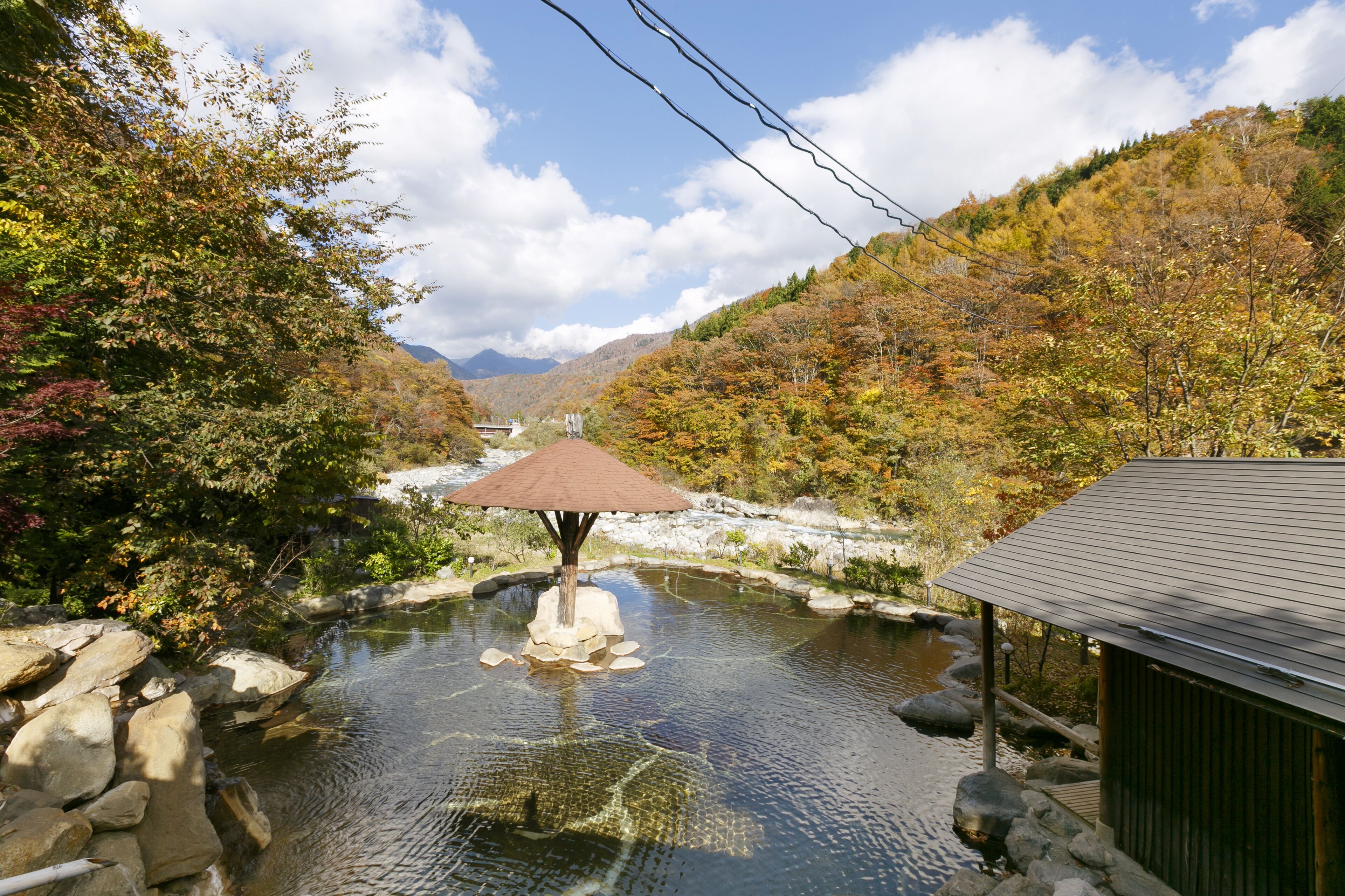 A traditional Japanese onsen with a wooden structure, a stone basin, and a view of a mountainous landscape.