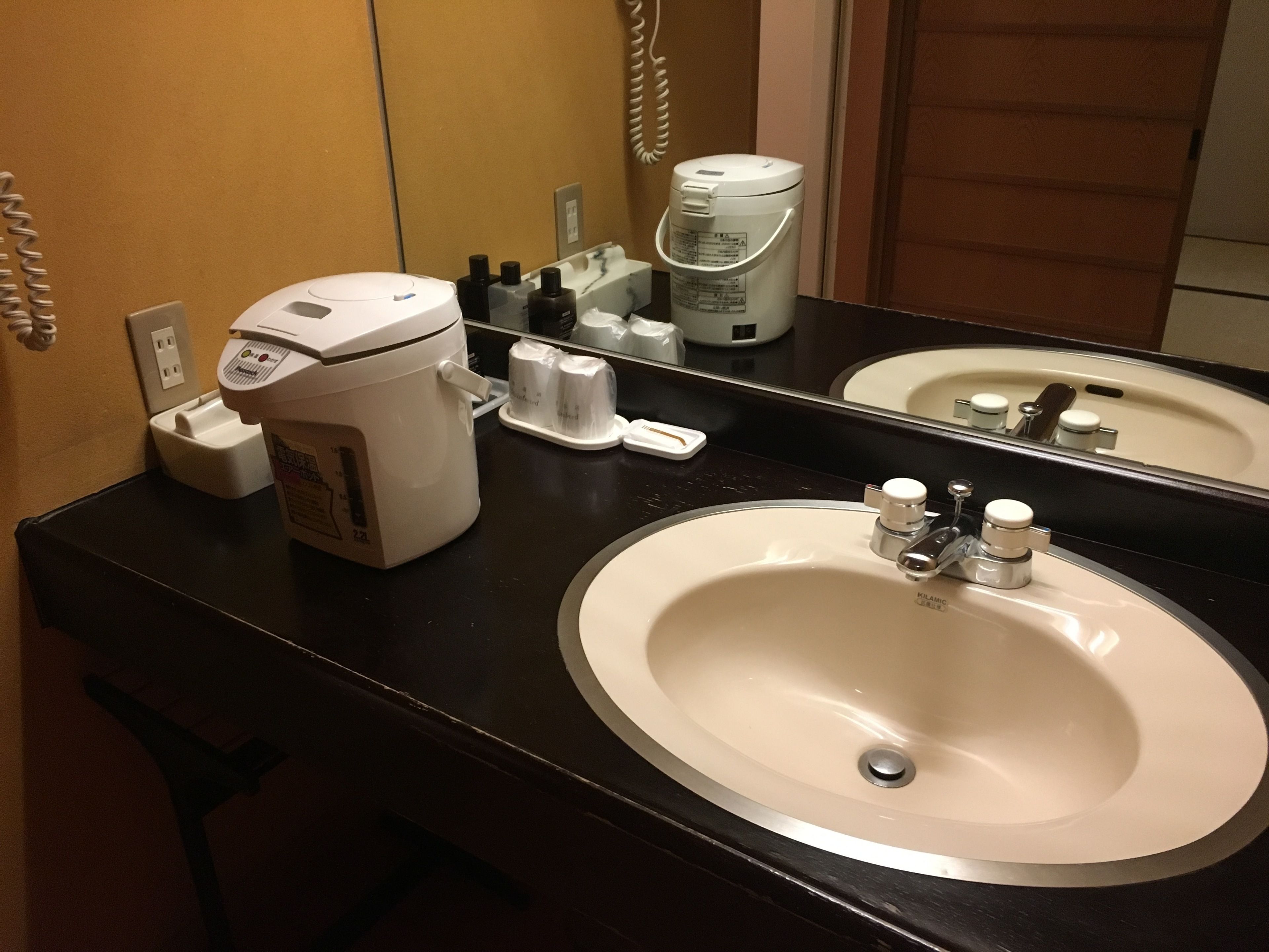Un baño de hotel con encimera negra, lavabo blanco y cafetera.