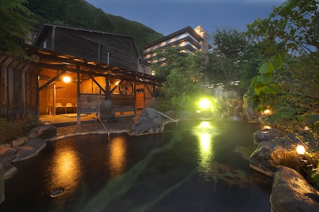 A traditional Japanese ryokan with a wooden exterior, a stone hot spring bath, and a view of a mountain in the background.