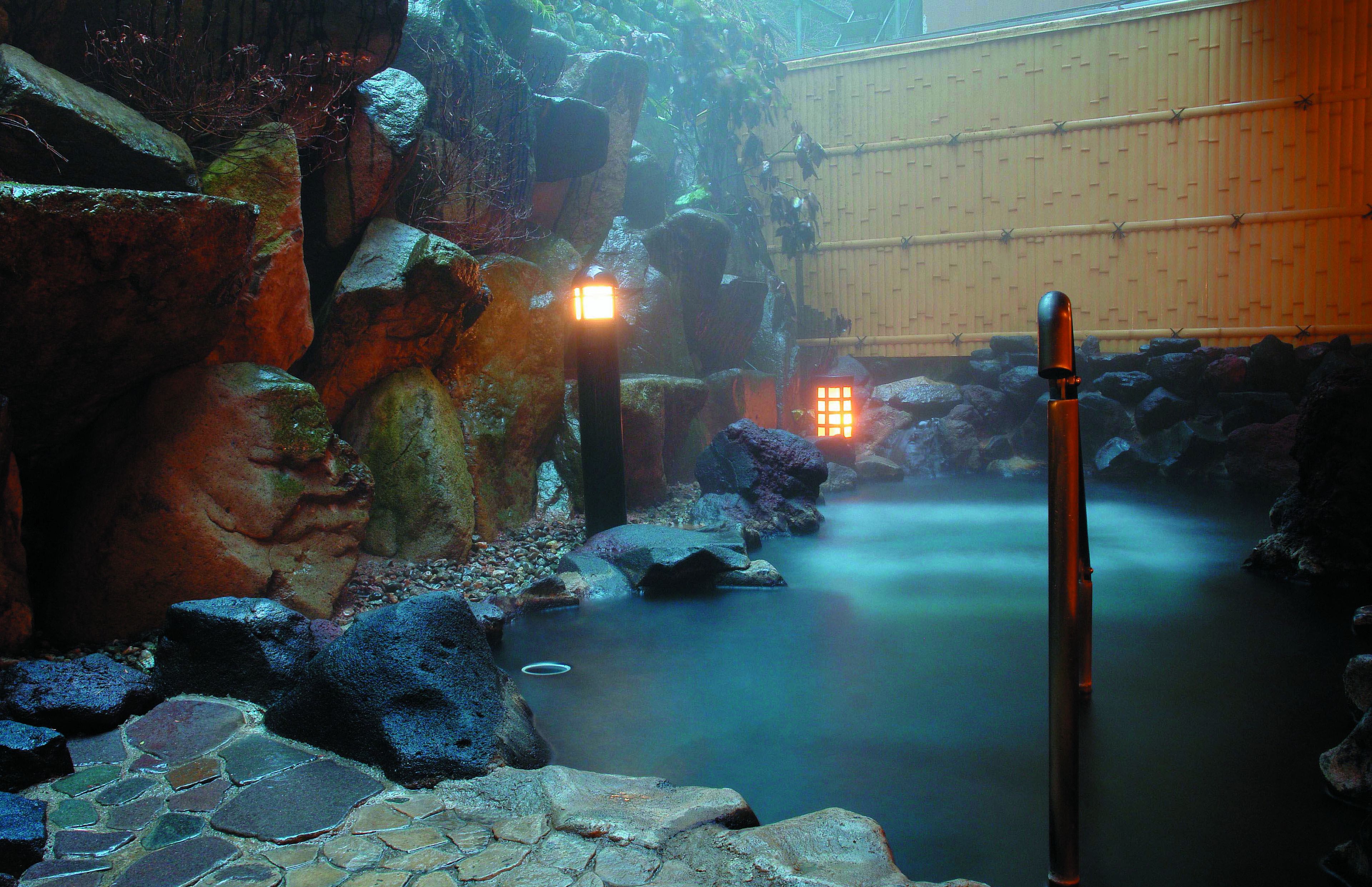 A serene indoor water feature with a stone pathway, illuminated lights, and a bamboo wall.