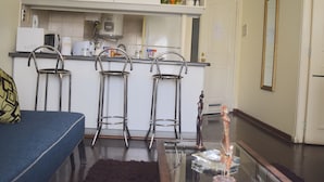 Un espace de vie compact comprenant un coin cuisine, un coin repas avec des tabourets de bar et un canapé.