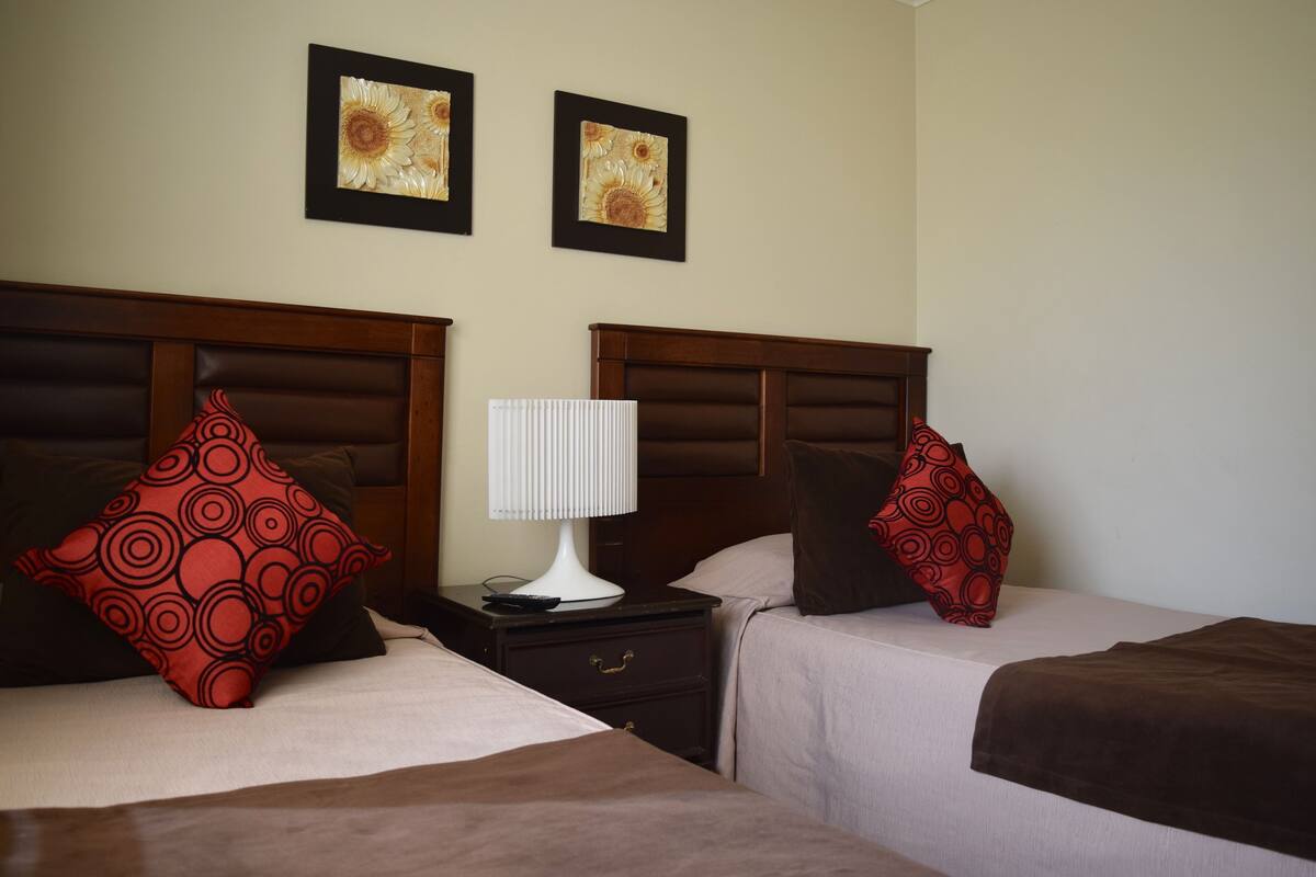 Two beds with headboards, a nightstand with a lamp, and two framed pictures on the wall.