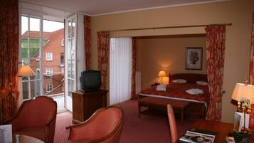 Una habitación de hotel con una cama, televisión, escritorio con lámpara y una silla.