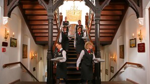 A grand staircase with a chandelier, framed artwork, and a sign indicating a reception area.
