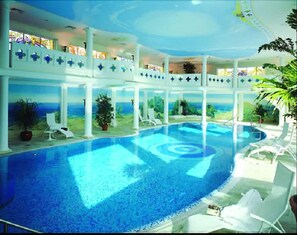 A large indoor swimming pool with a view of the ocean, surrounded by white columns and lounge chairs. - Genießer Hotel Altes Gymnasium (Husum)