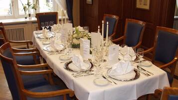 Mesa formal para comedor con mantel blanco, cubiertos y velas, rodeada de sillas tapizadas en azul en una habitación con paneles de madera.