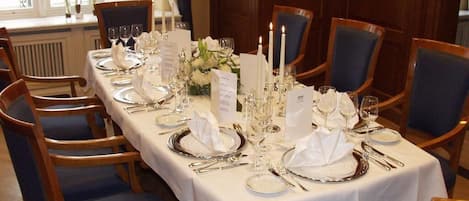 Mesa formal para comedor con mantel blanco, cubiertos y velas, rodeada de sillas tapizadas en azul en una habitación con paneles de madera.
