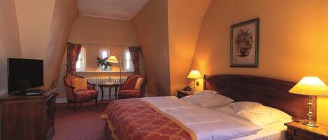 Habitación de hotel con una cama grande, televisor, escritorio con silla y ventana con cortinas.