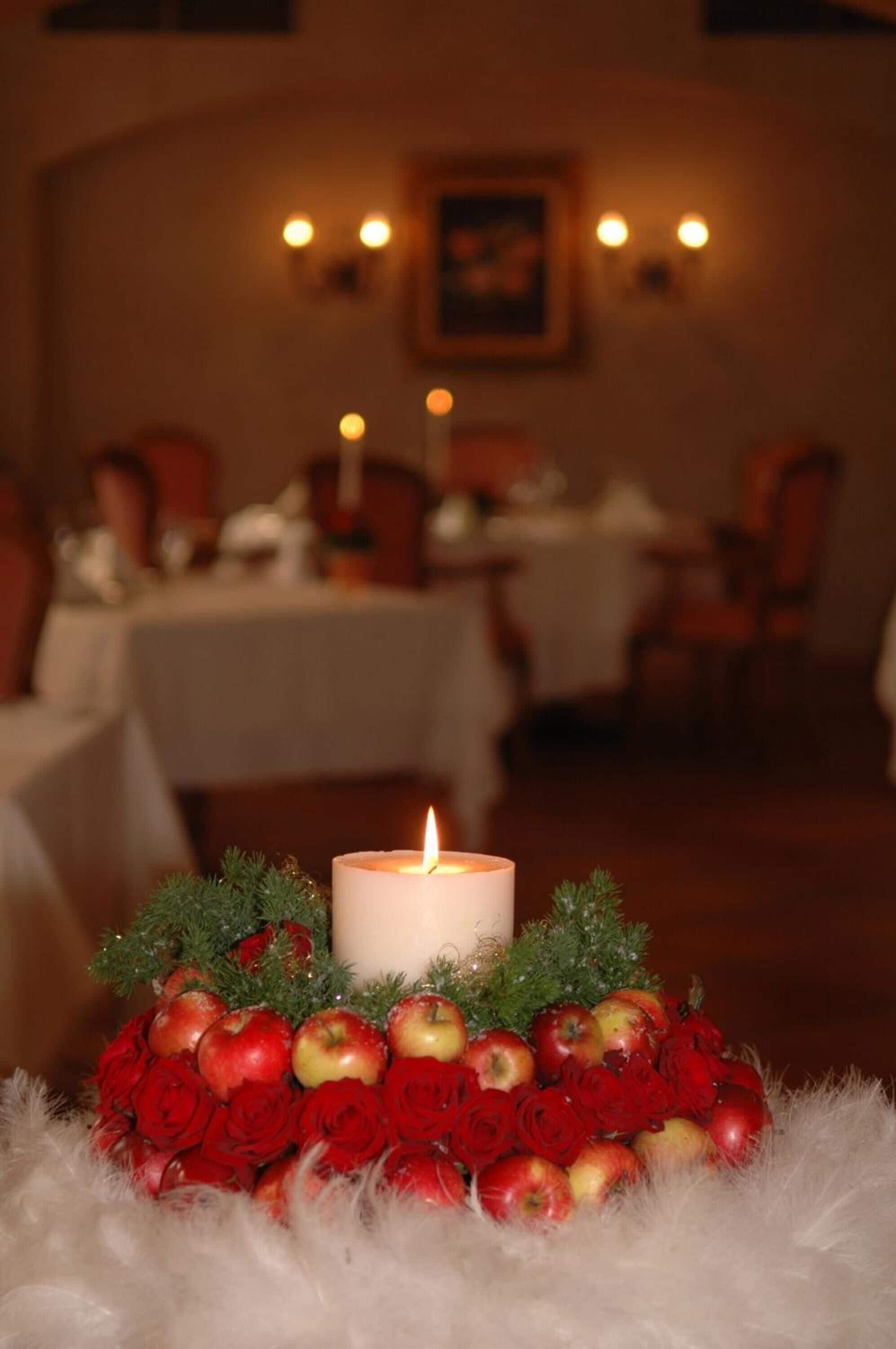 Un centro de mesa con velas, rosas rojas y manzanas sobre una superficie blanca y mullida.