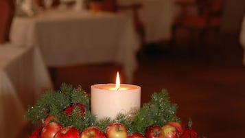 A candle centerpiece with red roses and apples on a white fluffy surface.