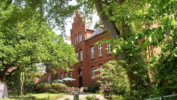 A red brick building with a tower, surrounded by lush greenery and a fenced courtyard.