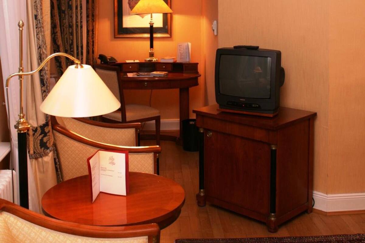 Een hotelkamer met een houten bureau, een televisie, een lamp en een ingelijst schilderij aan de muur.