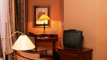 Una habitación de hotel con un escritorio de madera, un televisor, una lámpara y un cuadro en la pared.