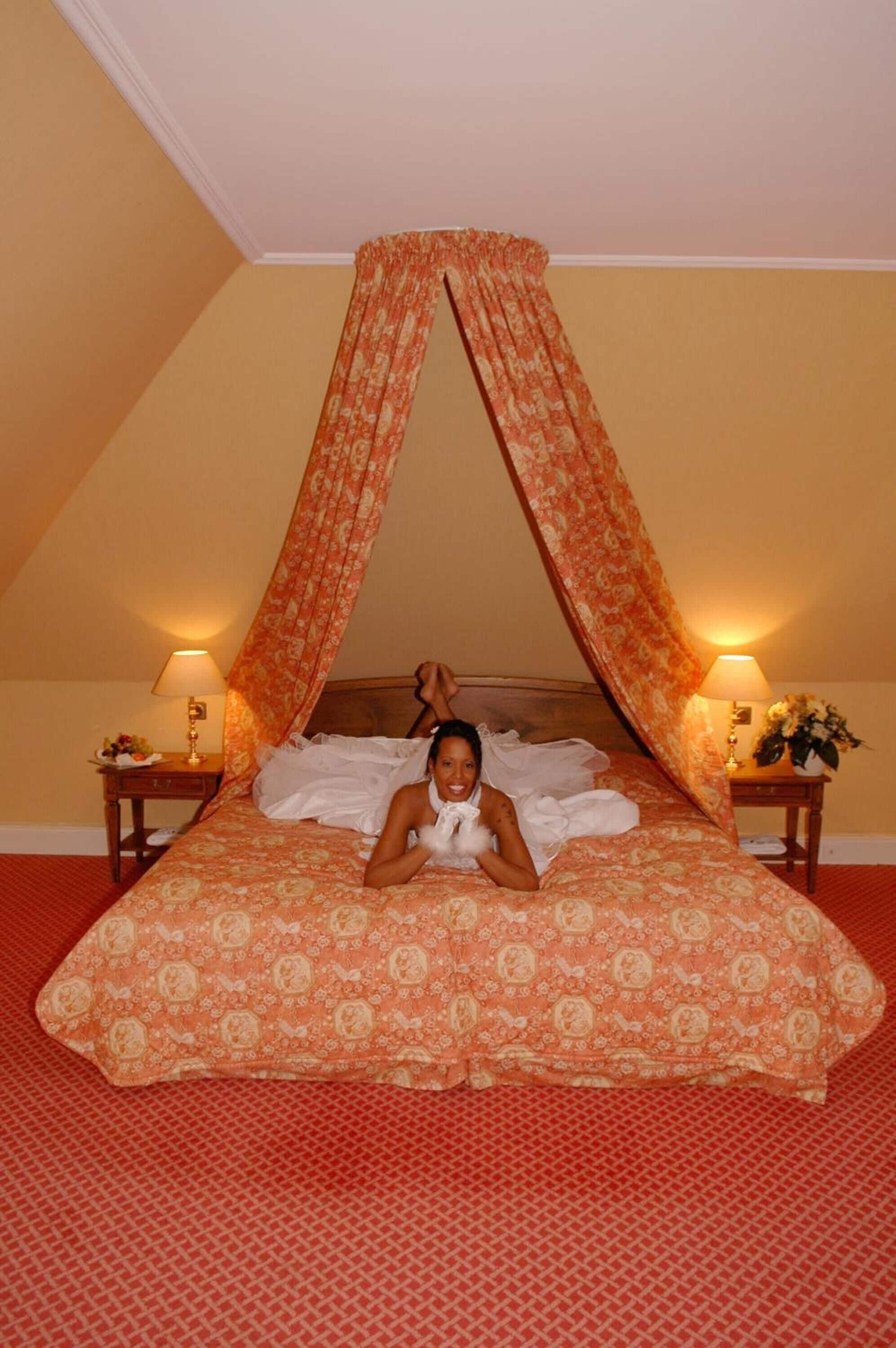 A bed with a canopy, a nightstand with a lamp, and a floral arrangement on the nightstand.