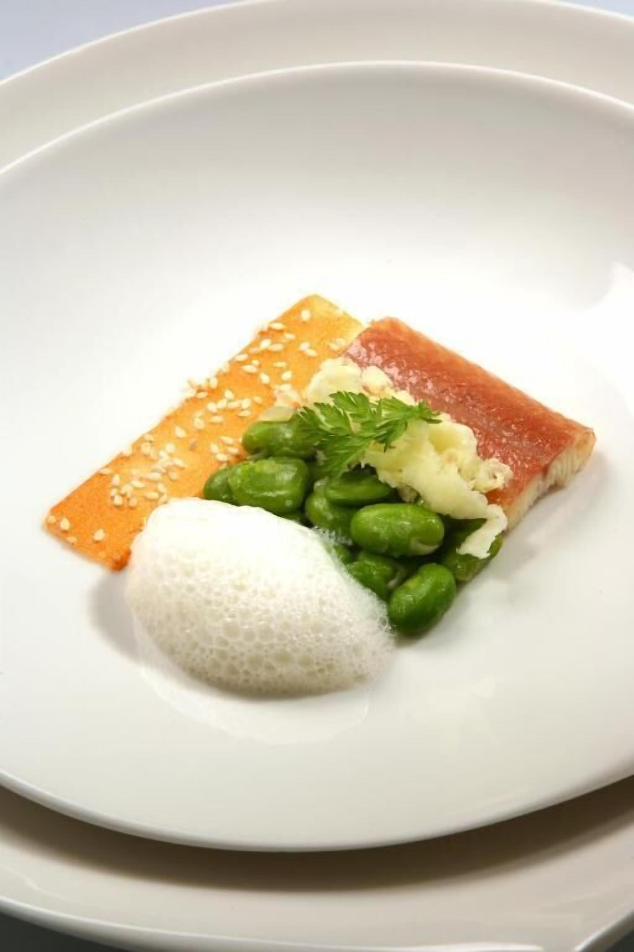 A white plate with a piece of salmon, a small portion of rice, and green peas.