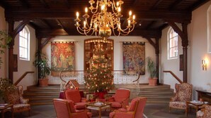 A grand lobby with a large chandelier, a Christmas tree, and red upholstered chairs.