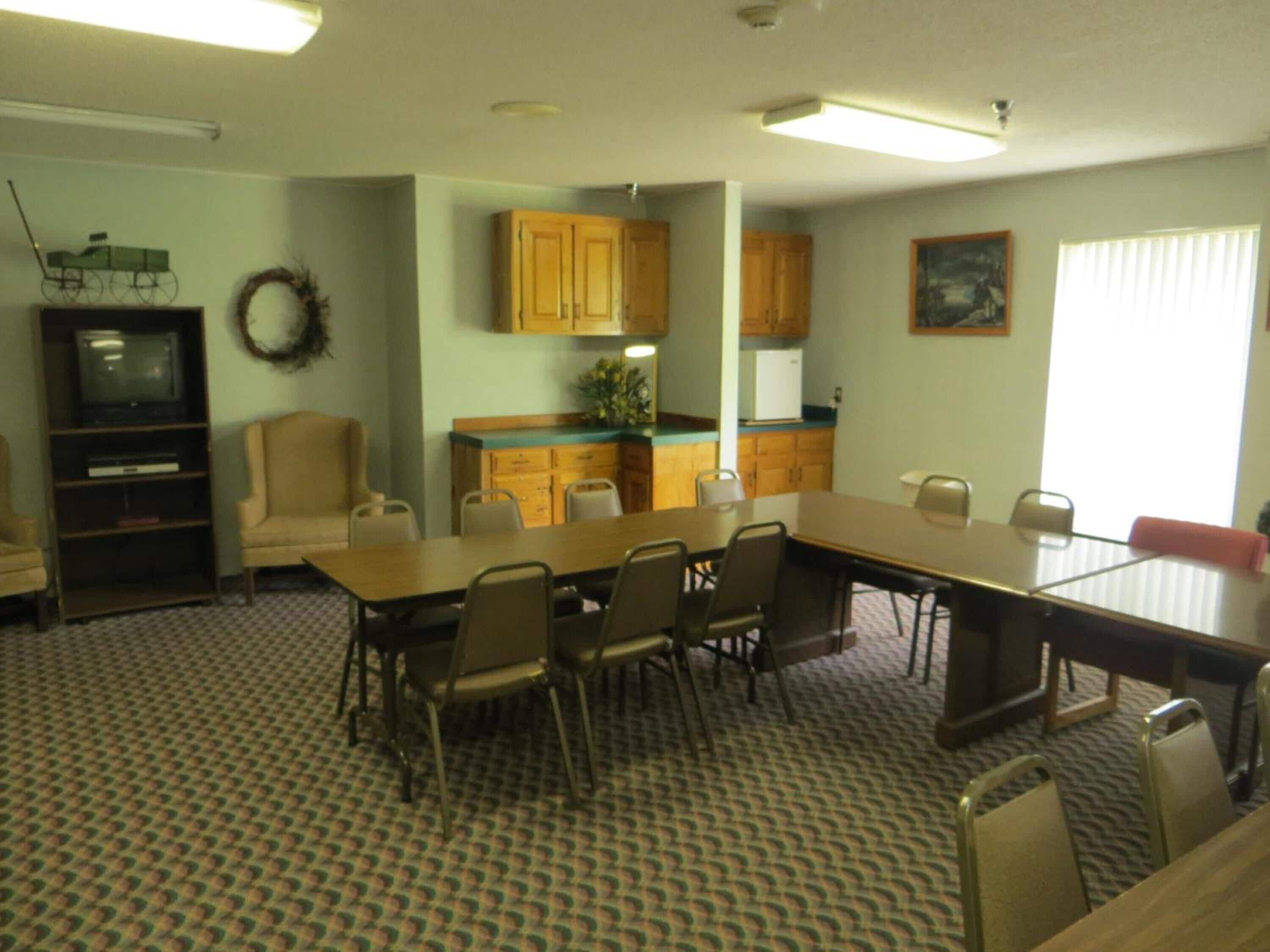 A conference room with a long table and chairs, a kitchenette, a television, and a wreath on the wall.