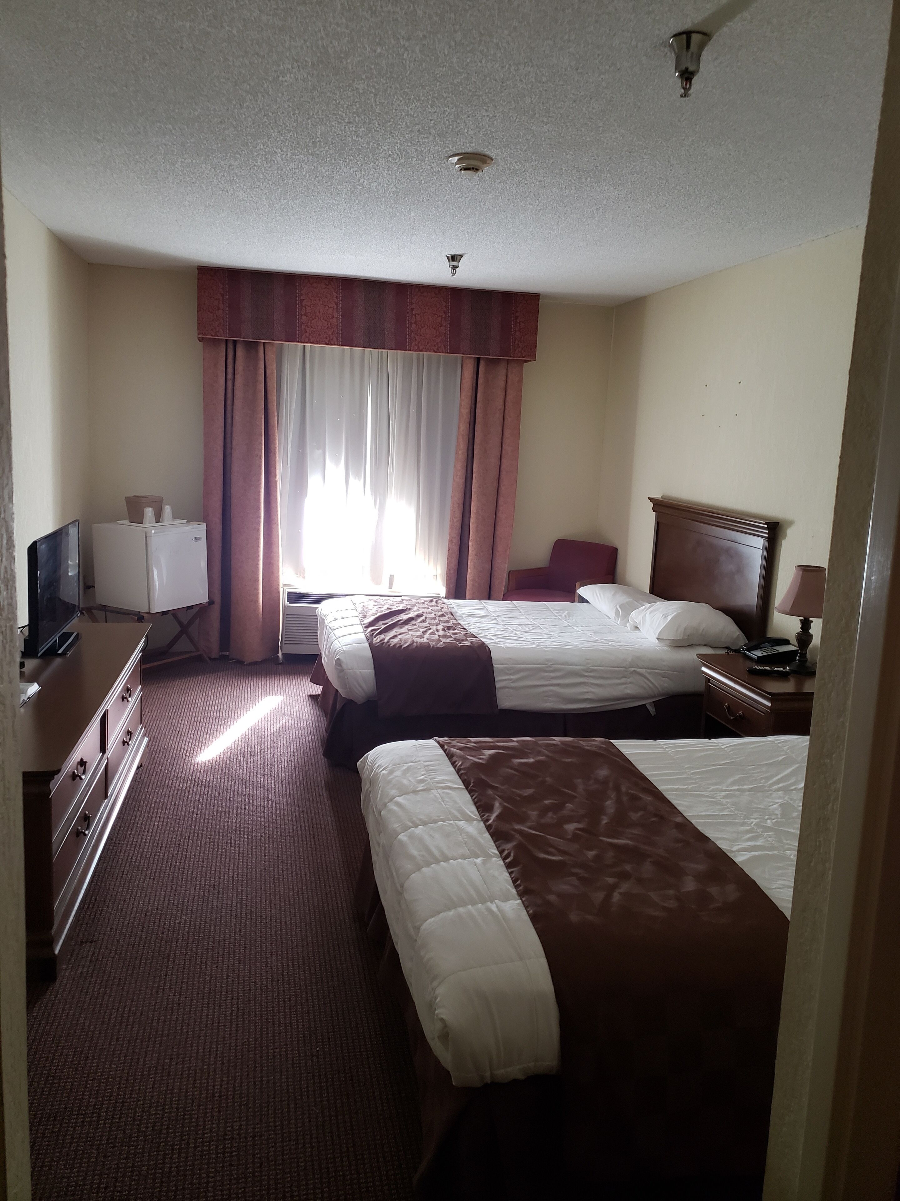 A hotel room with two beds, a desk with a television, a dresser, and a window with curtains.