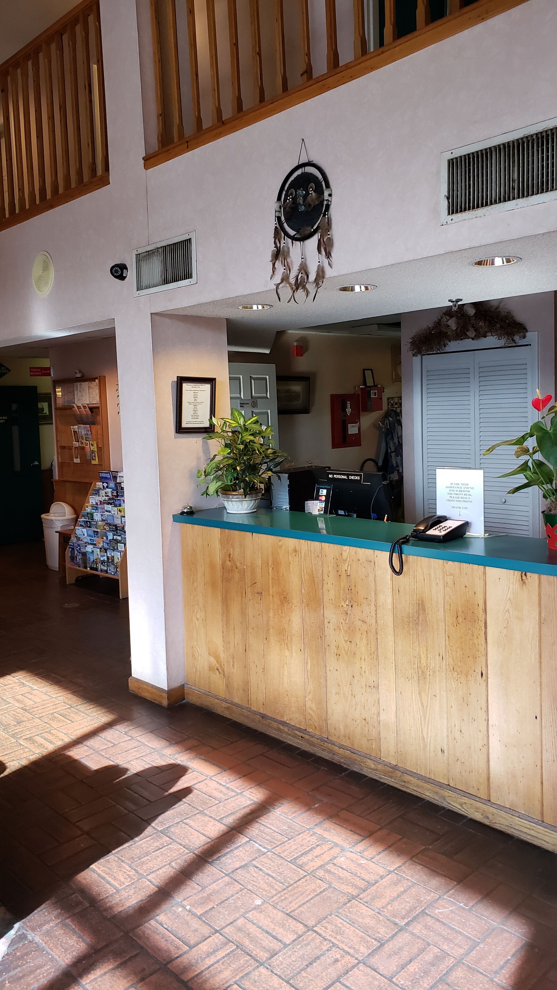 A reception desk with a wooden counter, a potted plant, a phone, and a sign.