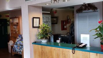A reception desk with a wooden counter, a potted plant, a phone, and a sign.