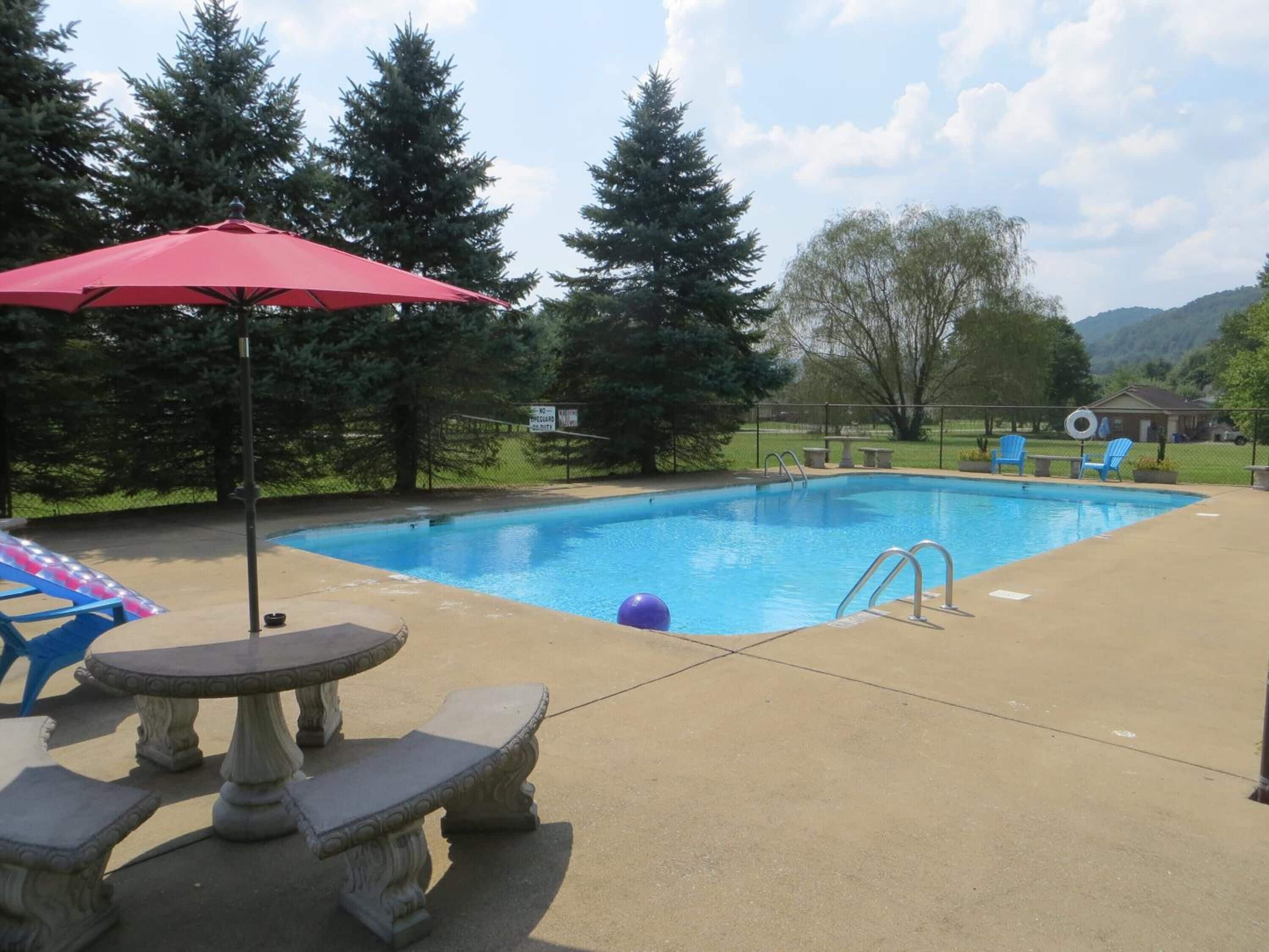 A rectangular swimming pool with a red umbrella, surrounded by trees and a view of hills.