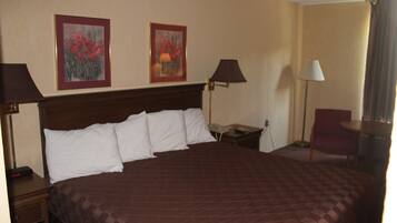A hotel room with a large bed, two wall-mounted lamps, a chair, and two framed floral paintings.