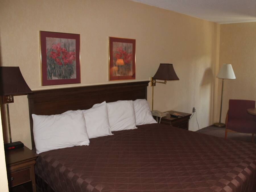 A hotel room with a large bed, two wall-mounted lamps, a chair, and two framed floral paintings.