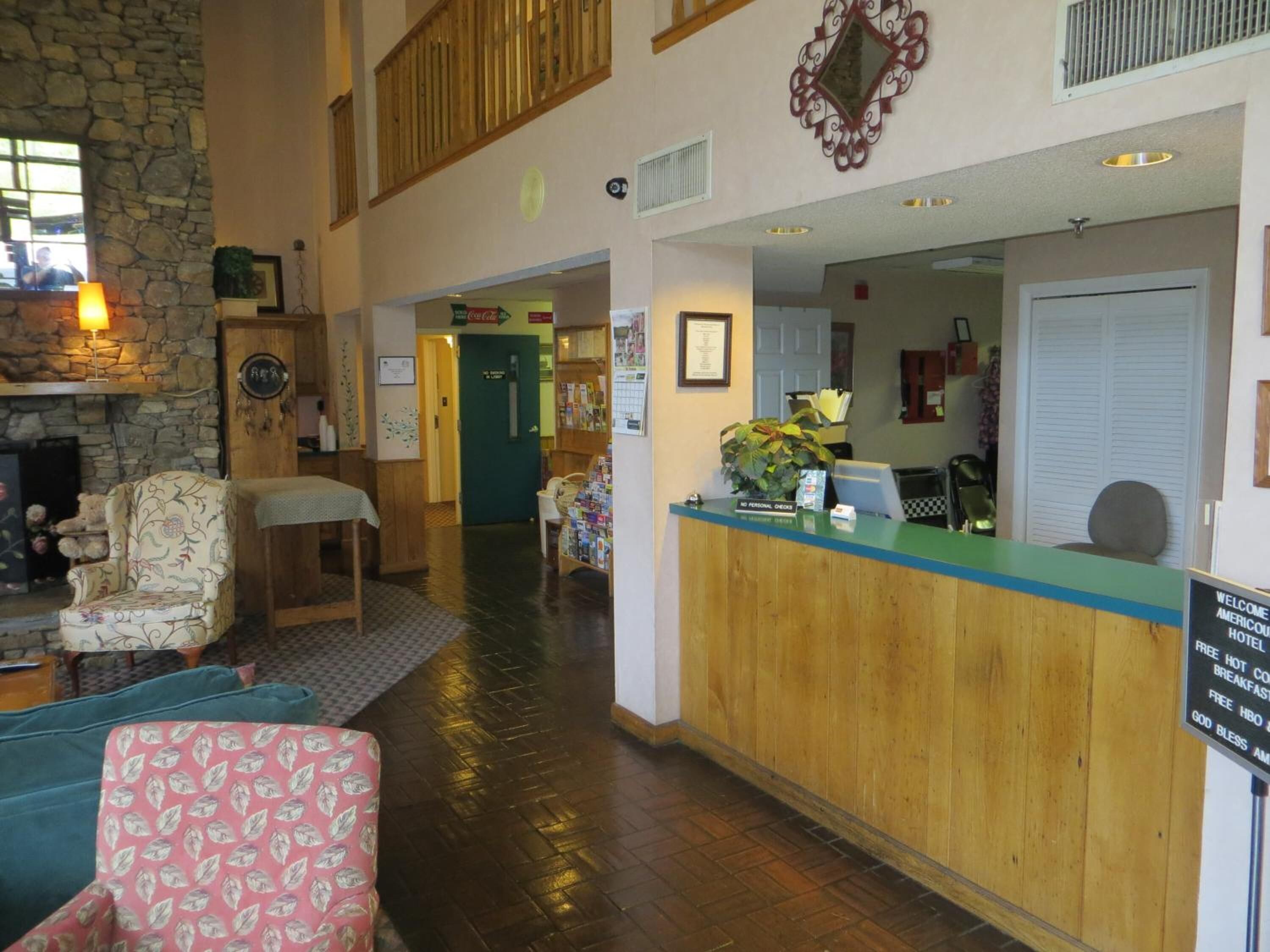 A hotel lobby with a wooden reception desk, a stone fireplace, and a high ceiling with wooden beams.