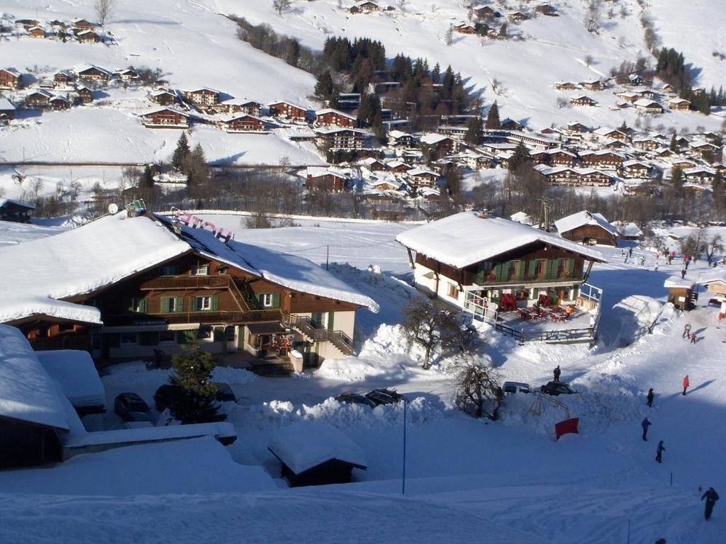 A snow-covered village with traditional wooden houses, a ski slope, and a clear view of the surrounding mountains.