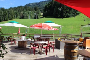 An outdoor deck with tables and chairs, umbrellas, and a wooden barrel. - Les Bernards (Praz-sur-Arly)