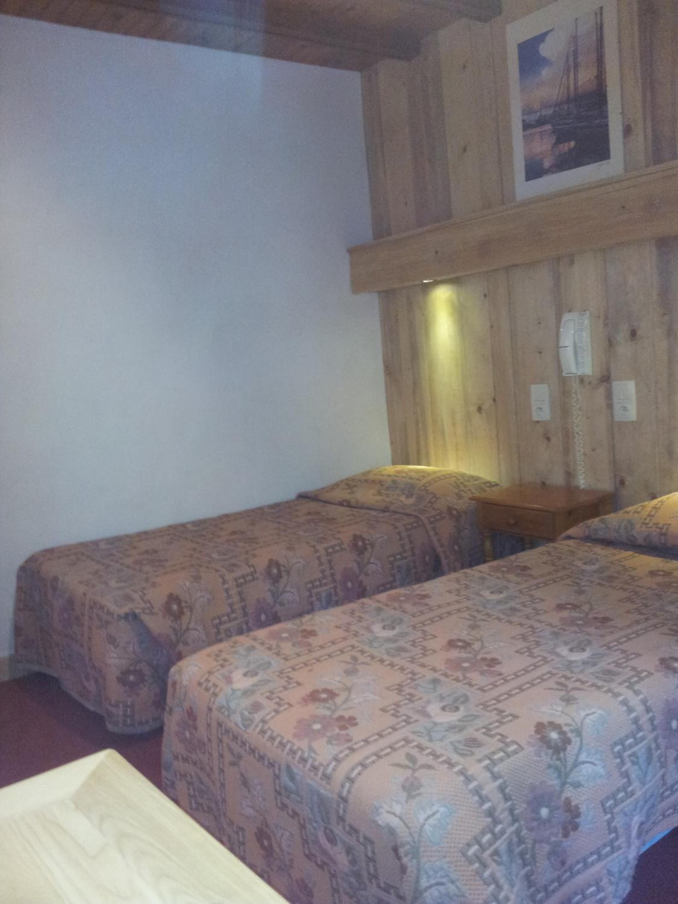 A room with two beds, wooden walls, and a small table with a lamp.
