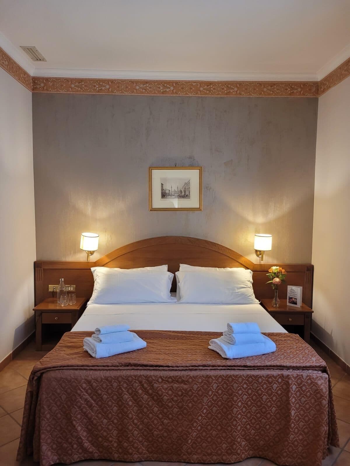 Une chambre d’hôtel avec un lit simple, deux tables de chevet, un tableau encadré au mur et une couverture de lit marron.