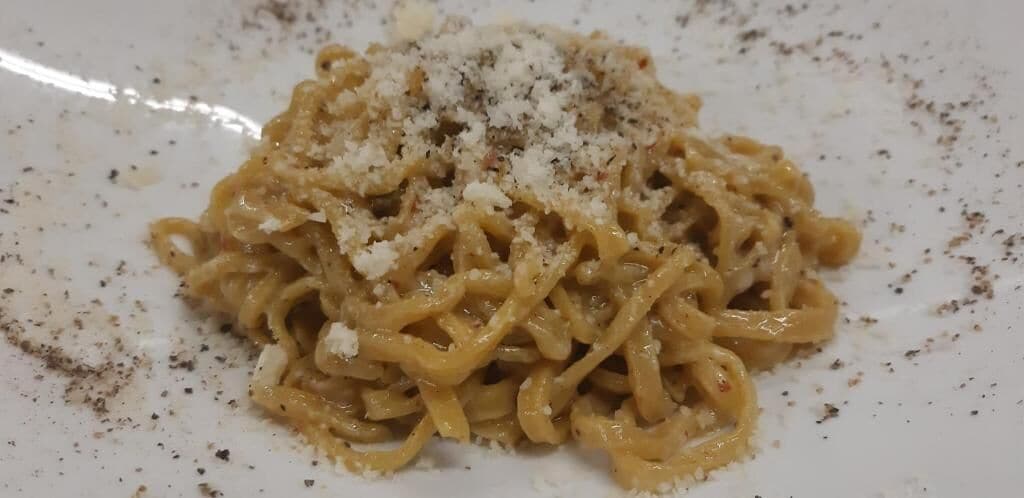 Um prato de massa com molho cremoso e queijo ralado por cima.