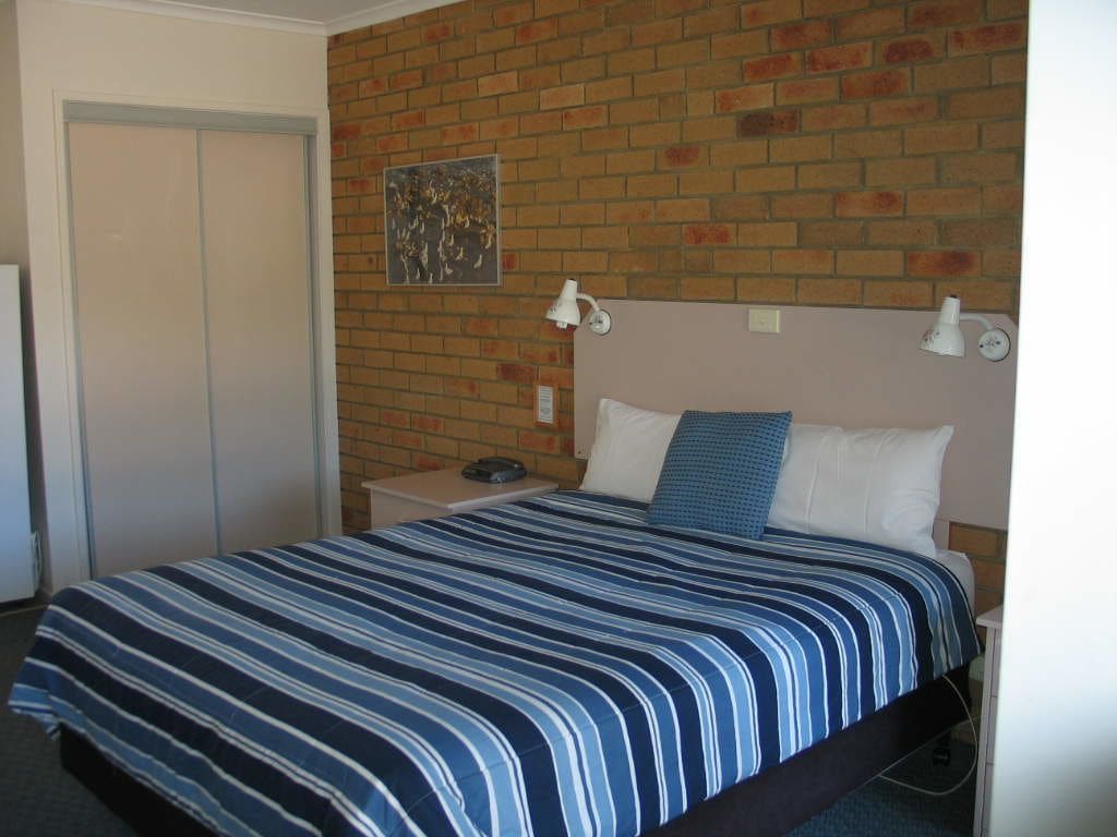 Un dormitorio con pared de ladrillo, una cama con colcha a rayas, dos lámparas de noche y una mesita de noche con un teléfono.