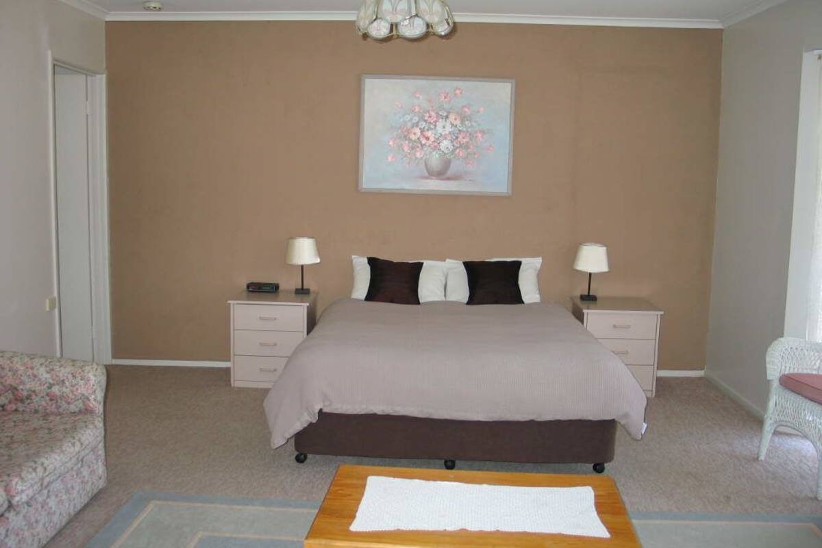 A bedroom with a bed, two bedside tables, a nightstand, a chair, and a painting on the wall.