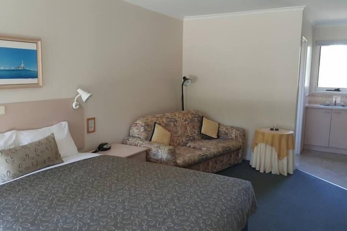 A hotel room with a bed, a sofa, a small table, a lamp, and a painting on the wall.