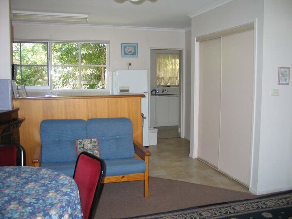 A compact room with a bed, a blue sofa, a small kitchen area, and a view of the outdoors through a window.