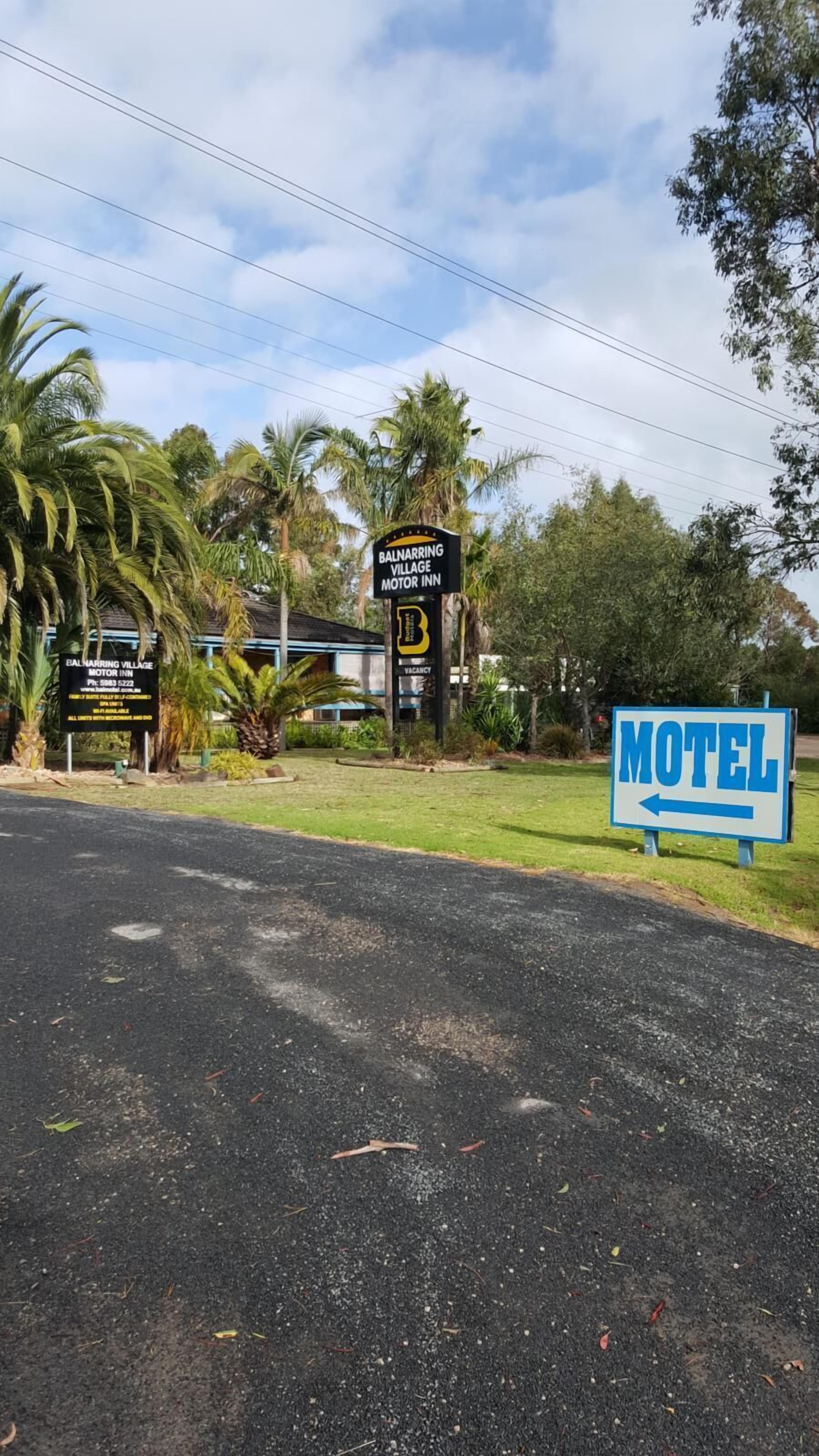 A motel sign with a directional arrow, palm trees, and a building with a signboard.