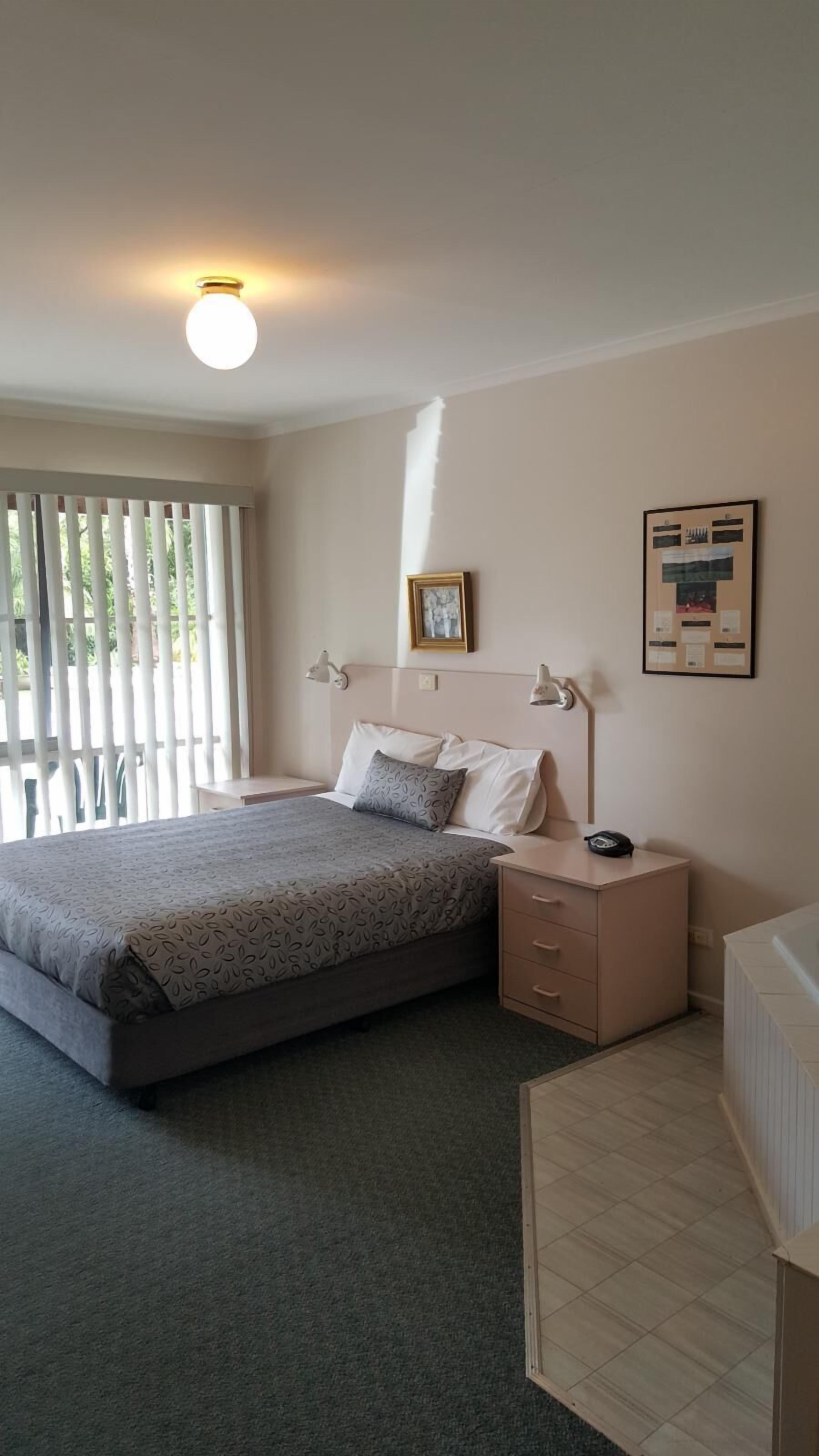 A bedroom with a bed, bedside tables, a nightstand, a framed picture, and a bulletin board on the wall.