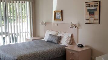 A bedroom with a bed, bedside tables, a nightstand, a framed picture, and a bulletin board on the wall.