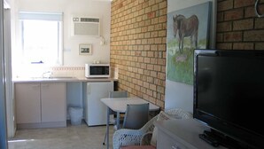A compact kitchen with a microwave, a refrigerator, and a dining area with wicker chairs. - Balnarring Village Motor Inn (Balnarring)