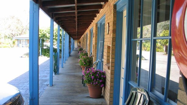 A covered outdoor area with a bench, potted plants, and a car parked nearby. - Balnarring Village Motor Inn (Balnarring)