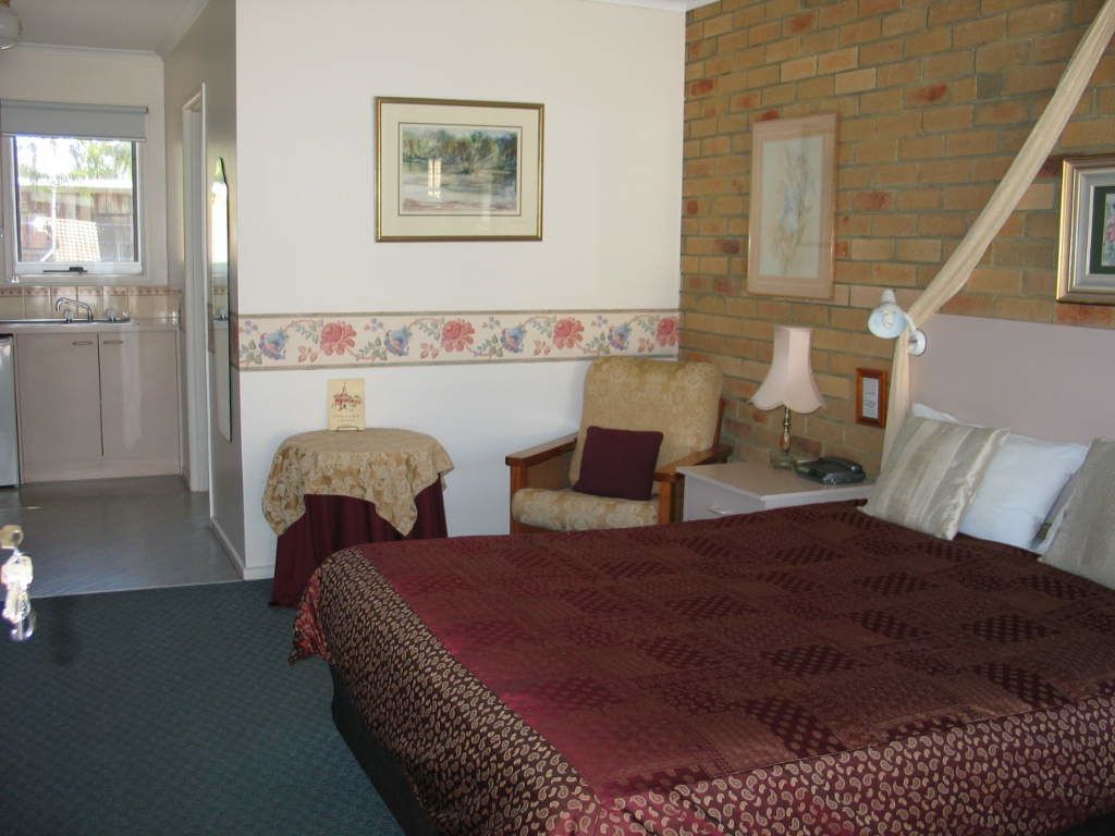 Habitación de hotel con una cama grande, una silla, una mesita de noche con lámpara y una ventana.