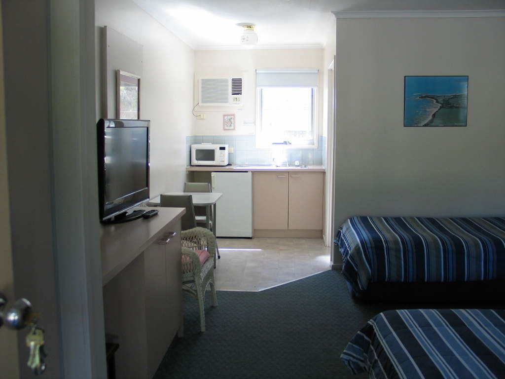 Habitación de hotel compacta con kitchenette, televisor, cama y ventana con vistas.